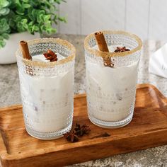 two glasses filled with white liquid sitting on top of a wooden tray