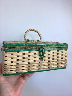 a hand holding a green and white wicker box with handles on it's side