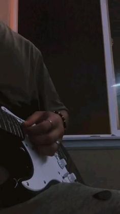 a man playing an electric guitar in front of a window