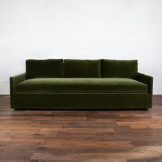 a green couch sitting on top of a hard wood floor next to a white wall