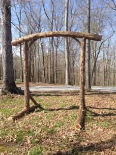 a wooden arch made out of logs in the middle of a forest with no leaves on it