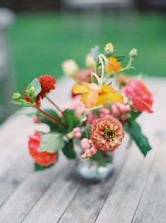 a glass vase filled with flowers on top of a wooden table next to green grass