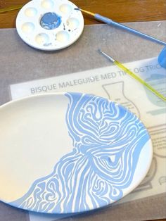 a white and blue plate sitting on top of a table next to paintbrushes