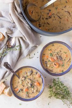 three bowls filled with soup next to a pot of bread and spoons on a table