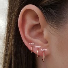 a woman's ear is shown with two small gold hoop earrings