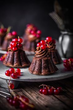 small cakes with chocolate frosting and cherries on a metal tray next to forks