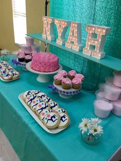 a table topped with cakes and cupcakes next to a neon sign that says nay