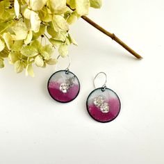 two purple and white earrings sitting on top of a table next to a flower pot