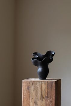 a black sculpture sitting on top of a wooden block in front of a wall and floor