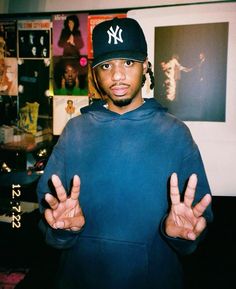 a young man wearing a new york yankees cap and hoodie holding his hands up