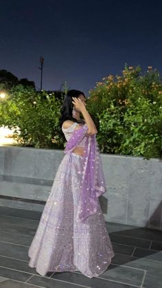 a woman in a purple sari is standing outside at night with her hand on her face