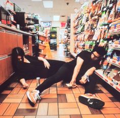 two people sitting on the floor in a grocery store, one is holding onto another person's leg