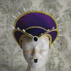 This royal Tudor inspired headdress is covered with silk shantung in either purple (pictured) or black.It is embellished with golden cord trimming all around the edges.It is further trimmed with pearl bead details that create a halo effect. The piece is completed with a beautiful crystal and pearl handmade element at the center front. The base is a headband style, completely handmade to be able to support the shape and design of the headdress. The adjustable elastic, that goes under the hair at Fitted High Crown Costume Hats And Headpieces, Fitted Costume Hat With Tall Crown, Fitted Tall Crown Costume Hats, Fantasy Costume Hat With Pinched Crown For Costume Party, Fantasy Costume Headpiece With Pinched Crown, Fantasy Headpieces For Mardi Gras Costume, Fantasy Headpieces For Costume Festivals, Fantasy Costume Headpiece For Mardi Gras, Fitted Tall Crown Costume Hat For Costume Party