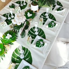 the table is set with green and white plates, place settings, and palm leaves