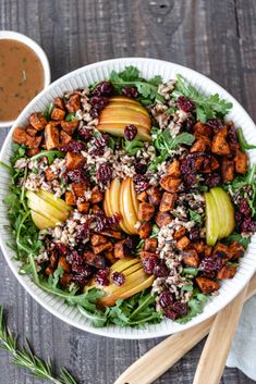 a salad with apples and cranberries in a white bowl next to dipping sauce