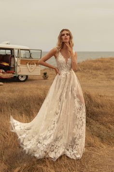 a woman in a white dress standing on top of a dry grass field next to an old v - neck camper