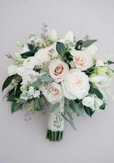 a bridal bouquet with white flowers and greenery is displayed on a gray background