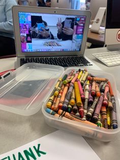 an open laptop computer sitting on top of a desk next to lots of crayons