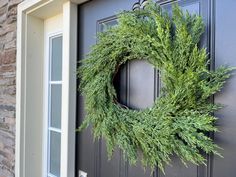 a wreath is hanging on the front door of a house that has been decorated with greenery