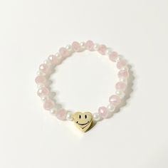 a bracelet with a smiley face on it and pink pearls around the wrist, along with a gold heart charm