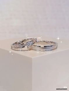 two wedding rings sitting on top of a white box with sparkles in the background