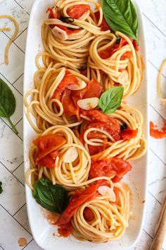 pasta with tomato sauce and basil leaves on a white platter next to chopsticks