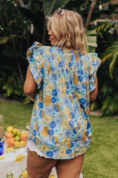 - Embrace feminine florals this season with this sweet top! - Unlined material with a colorful floral print - A ruffled v-notched neckline - A smocked upper bodice - Short flutter sleeves - A relaxed silhouette that ends in a rounded hemline Garden Party Tops With Flutter Sleeves And Floral Print, Blue Floral Print Tops With Ruffle Sleeves, Blue Ruffle Sleeve Tops For Vacation, Blue Bohemian Blouse With Ruffle Sleeves, V-neck Ruffle Top For Garden Party, Bohemian Blue Blouse With Ruffle Sleeves, Multicolor Ditsy Floral Print Tops For Vacation, Floral Print Ruffle Sleeve Blouse For Vacation, Bohemian Floral Print Tops For Garden Party