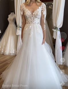 a woman standing in front of a mirror wearing a white wedding dress with sheer sleeves