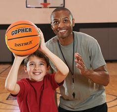 a man holding a basketball over his head while standing next to a young boy on a basketball court