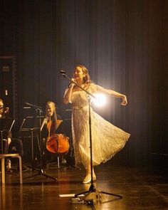 a woman in a white dress holding a microphone and standing next to other musicians on stage