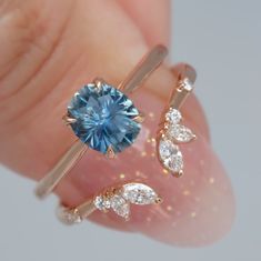 a close up of a person's hand holding two rings with a blue stone