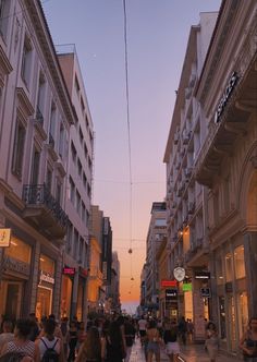 many people are walking down the street in front of buildings at sunset or dawn,