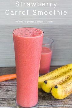 a pink smoothie in a tall glass next to bananas and carrots on a wooden table