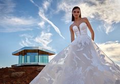 a woman in a white wedding dress standing on top of a hill next to a building