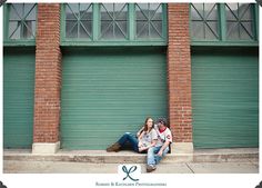 a man and woman sitting on the ground in front of a green garage door