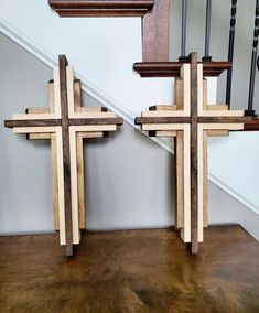 two wooden crosses sitting next to each other on top of a hard wood floor in front of a stair case