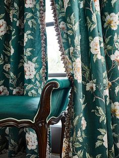 a chair sitting next to a window covered in green floral curtaines and drapes