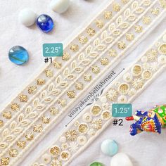 some beads are laying next to each other on a table with white lace and gold trimmings