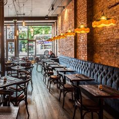 an empty restaurant with wooden tables and blue velvet bench seats, exposed brick walls and hanging lights