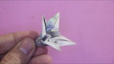 a hand holding an origami flower on top of a pink surface with white tips