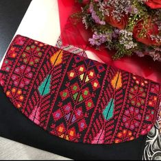 a red and black purse sitting on top of a table next to flowers in a vase