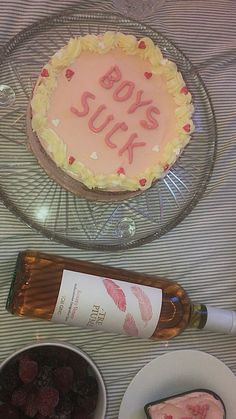 a cake with writing on it sitting next to bowls of fruit and a bottle of wine