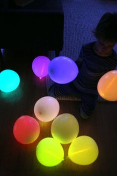 a young child sitting on the floor surrounded by glowing plastic balls in different colors and shapes