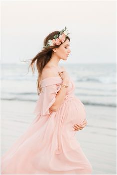 a pregnant woman wearing a flower crown standing on the beach