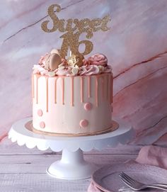 a pink and gold birthday cake on a white pedestal with a pink marble background that says sweet sixteen