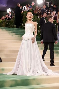 a woman in a white gown standing on steps with cameras around her and people taking pictures