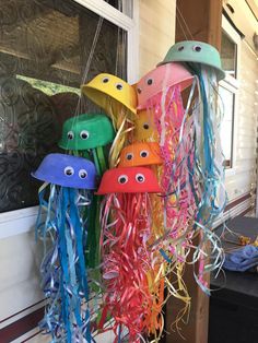 some very pretty colorful hats hanging from the side of a building with googly eyes on them