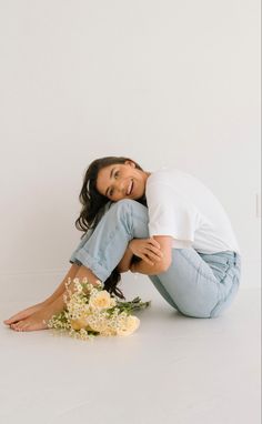 a woman sitting on the ground with flowers in front of her and smiling at the camera