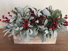 a wooden box filled with red berries and greenery on top of a wood table