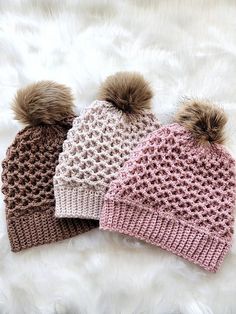 three knitted hats with pom - poms on top of white furnishing